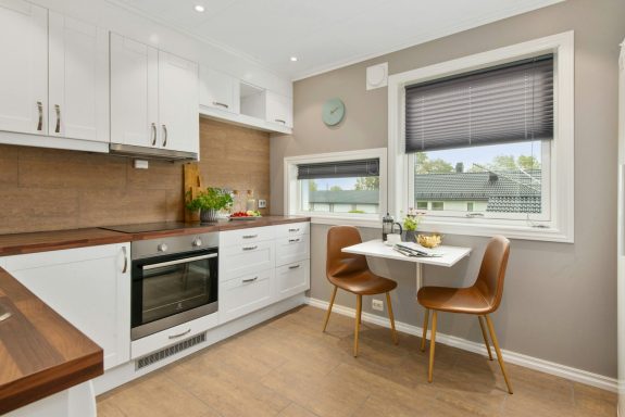 Cuisine moderne avec meubles blancs, table dinatoire et fenêtres lumineuses.